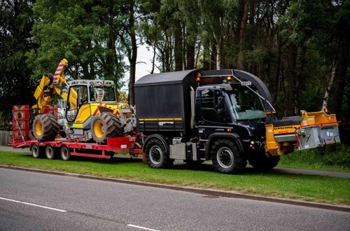 Unimog with tree shear and wood chipper towing Menzi Muck excavator for tree removalfor a commercial customer